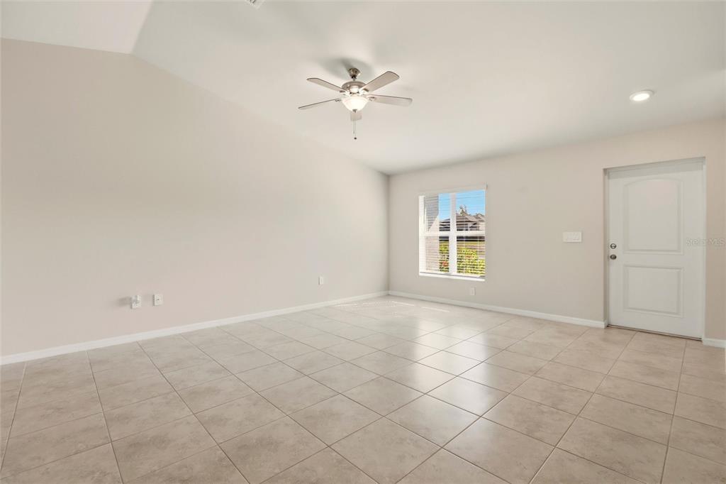A bright, empty living room features light-colored tile flooring, a ceiling fan, and a door — 3600 NE 20TH PLACE, CAPE CORAL, FL
