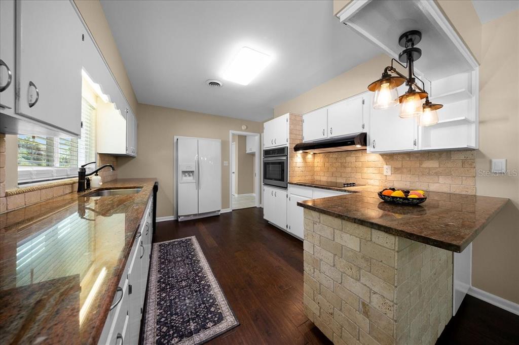 A kitchen features white cabinets, granite countertops, a brick-faced peninsula, and dark wood flooring — 2333 E FORT KING STREET, OCALA, FL