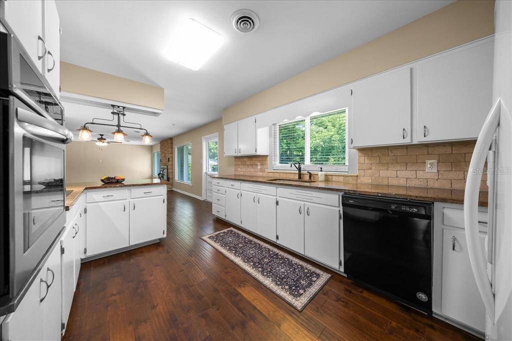 A kitchen features white cabinets, granite countertops, a brick backsplash, and dark hardwood flooring — 2333 E FORT KING STREET, OCALA, FL