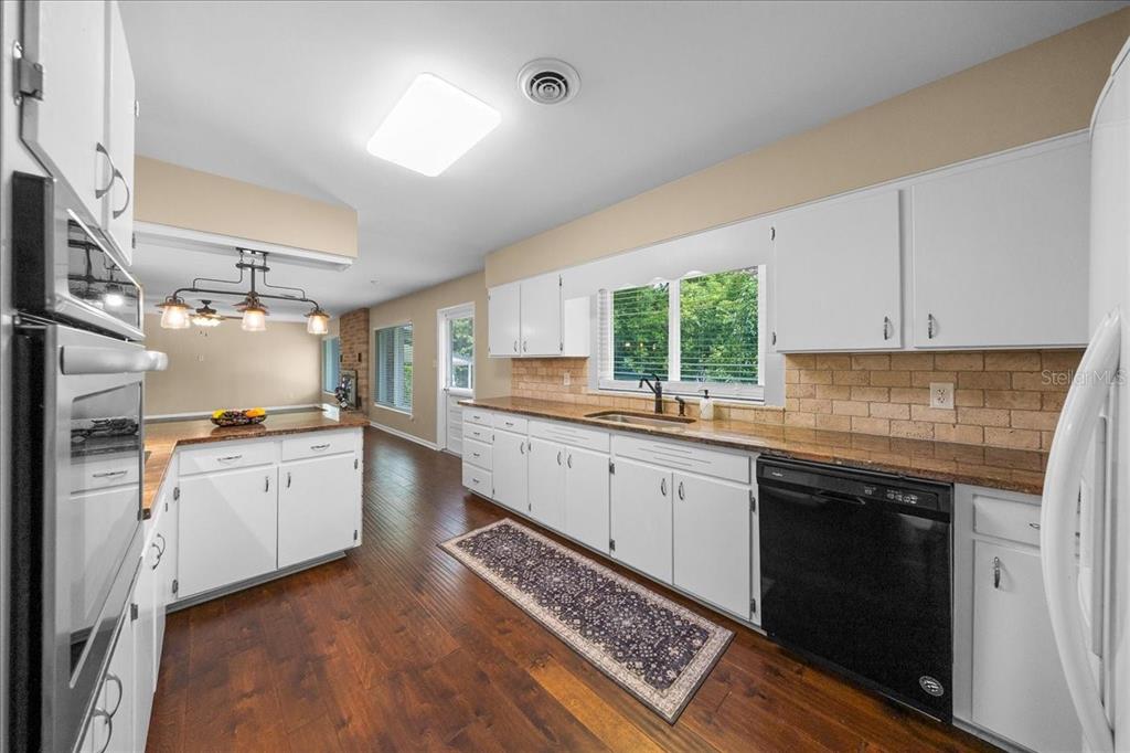 A kitchen features white cabinets, dark countertops, a black dishwasher, and hardwood flooring — 2333 E FORT KING STREET, OCALA, FL