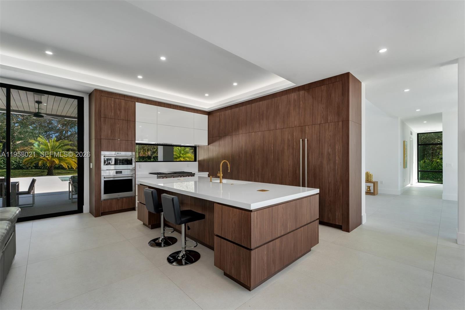 A modern kitchen features wood cabinetry, a white island, and a view of a patio — 9525 SW 95th Ct, Miami FL 33176, MIAMI, FL