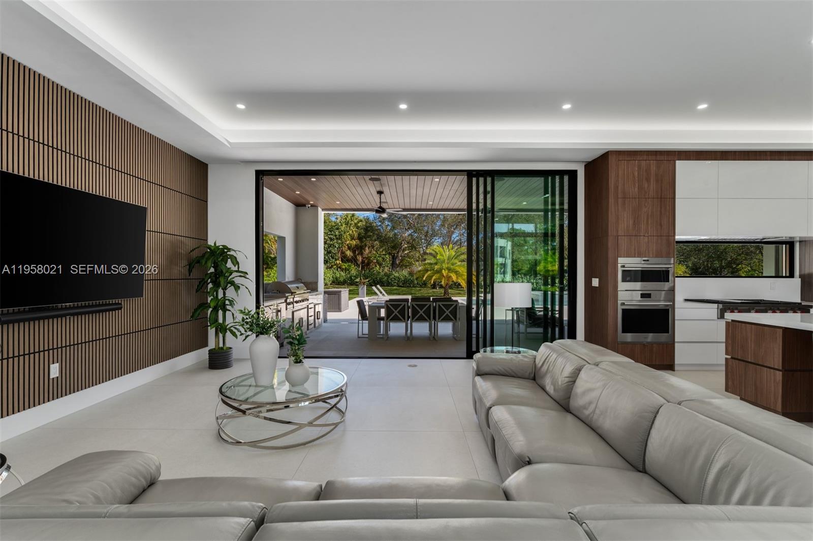 A modern living room features a slatted wood wall, large sliding doors, and outdoor dining — 9525 SW 95th Ct, Miami FL 33176, MIAMI, FL