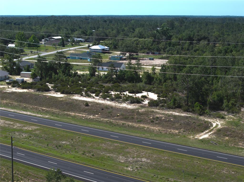 An aerial view shows a vacant lot adjacent to a multi-lane highway and nearby houses — 000 NE HWY 27 ALT, WILLISTON, FL