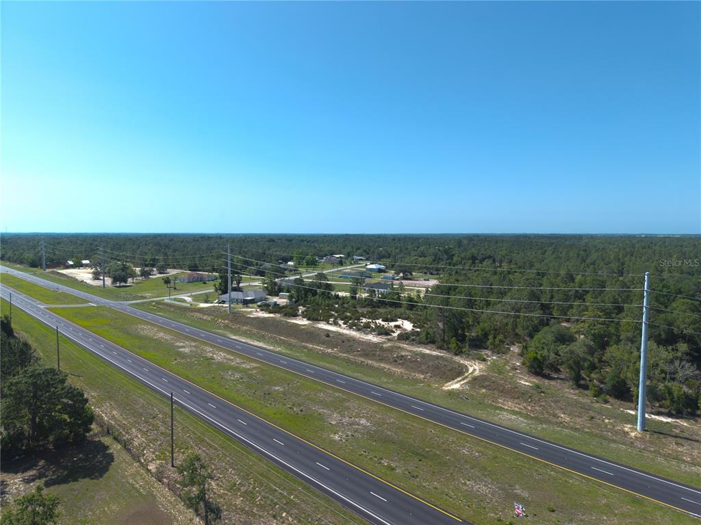 An aerial view shows a multi-lane highway running alongside a wooded area with scattered houses — 000 NE HWY 27 ALT, WILLISTON, FL