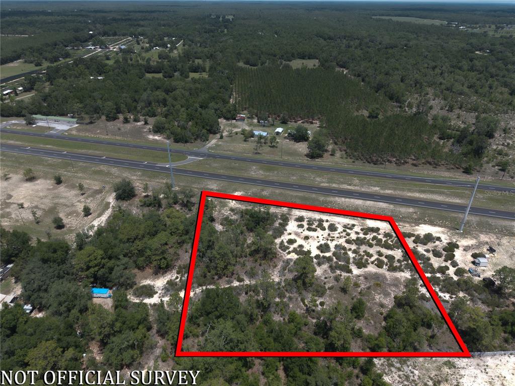 An aerial view shows a vacant, wooded lot outlined in red next to a highway — 000 NE HWY 27 ALT, WILLISTON, FL