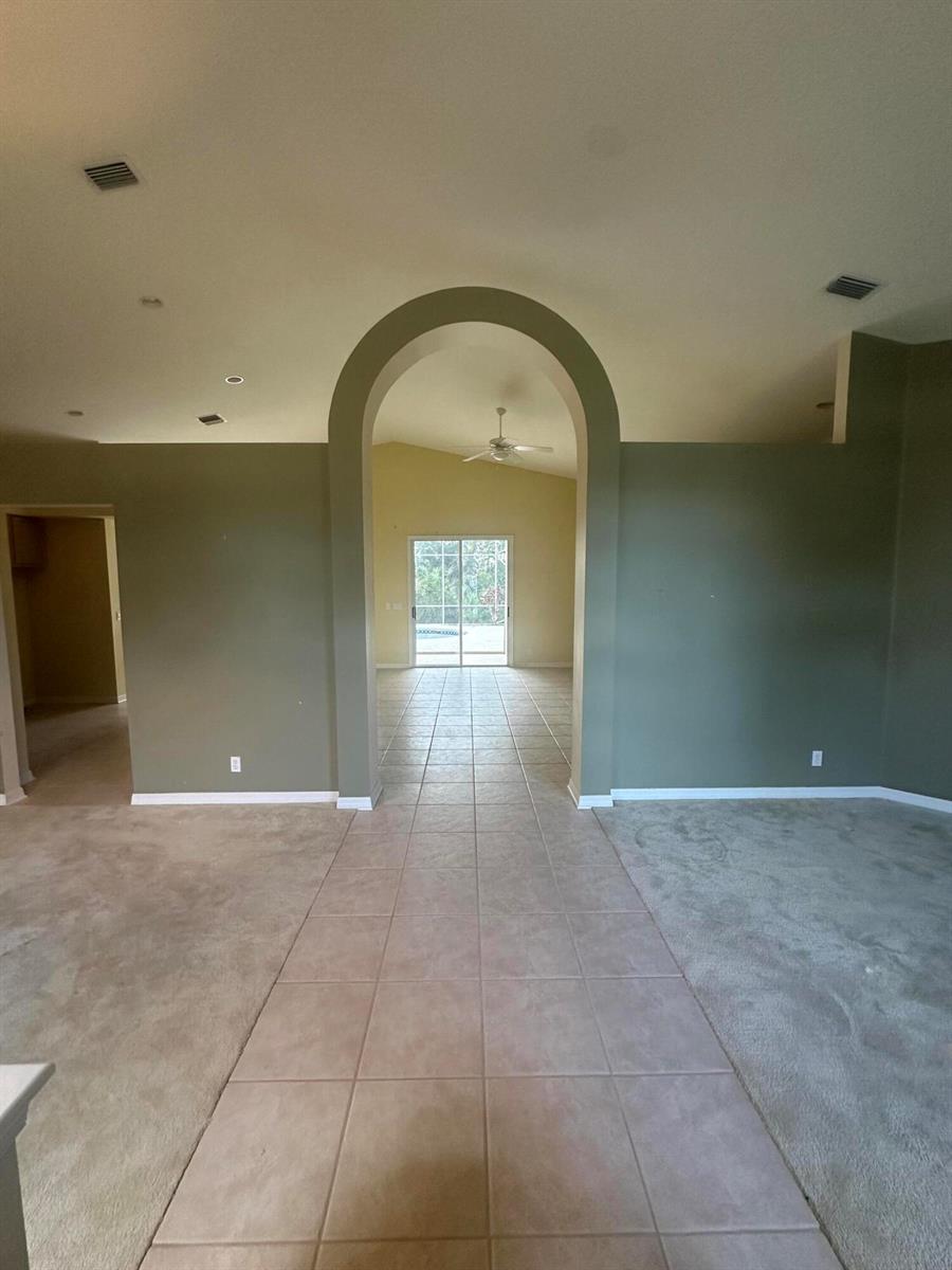 A view through an arched doorway shows a tiled walkway leading to a glass sliding door — 3102 NW Windemere Drive, Jensen Beach FL 34957, JENSEN BEACH, FL