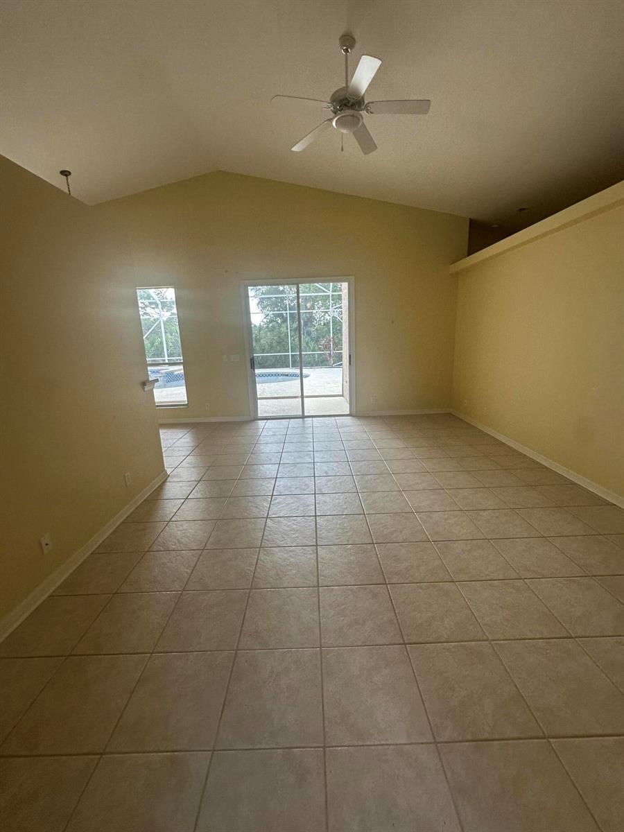 An empty room with beige tile flooring, a vaulted ceiling, and sliding glass patio doors — 3102 NW Windemere Drive, Jensen Beach FL 34957, JENSEN BEACH, FL