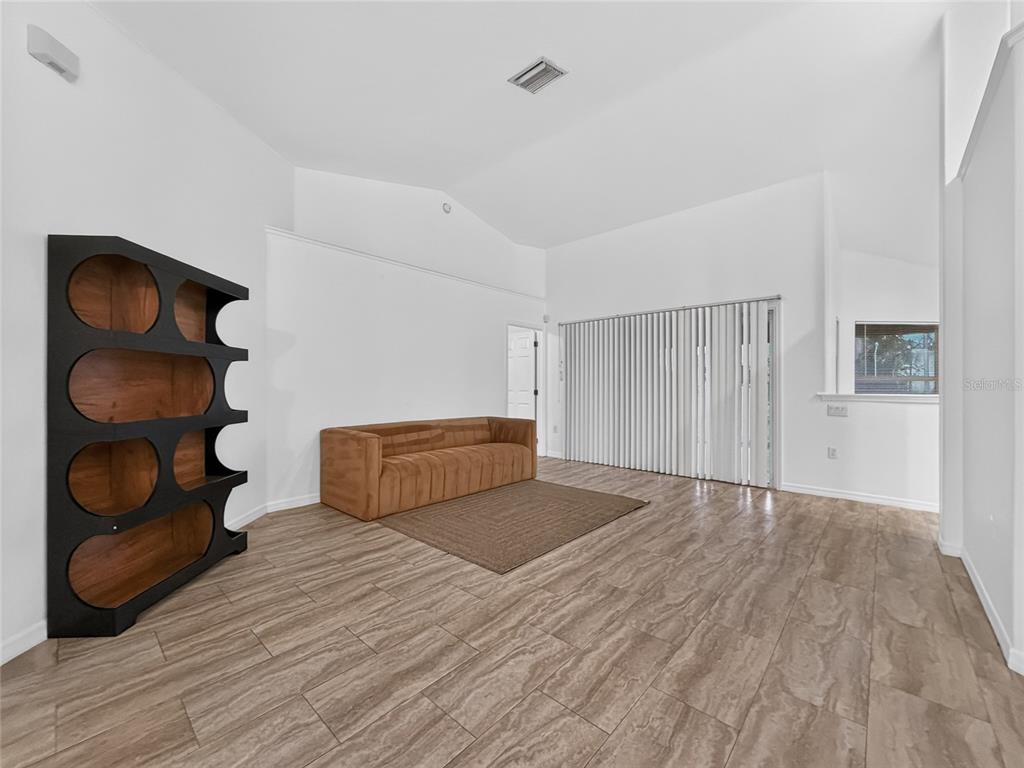 A living room with vaulted ceilings, wood-look tile flooring, a brown sofa, and a bookshelf — 13405 SW 86TH AVENUE, OCALA, FL