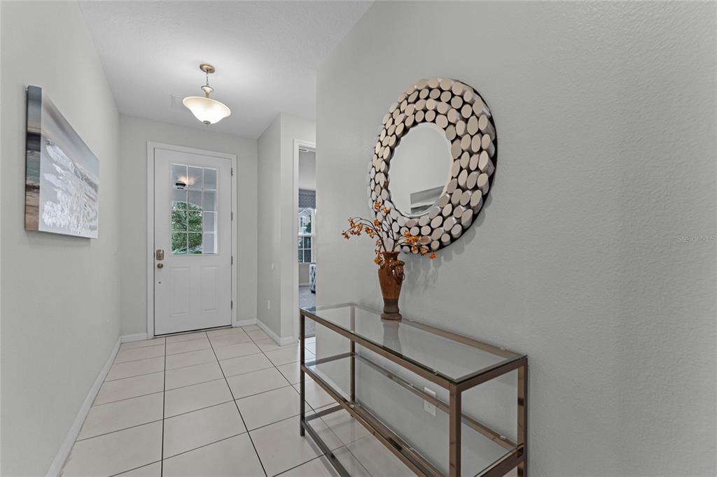 A tiled entryway features a glass console table, a decorative mirror, and a front door — 1754 CARIBBEAN VIEW TERRACE, KISSIMMEE, FL