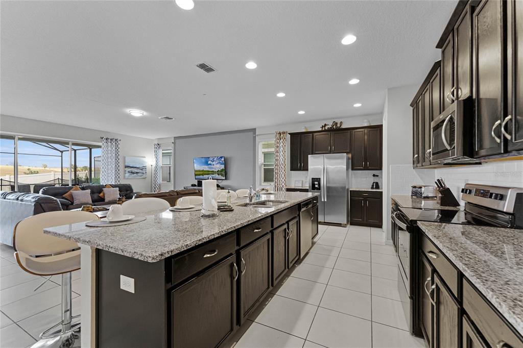 A kitchen with dark wood cabinets, granite countertops, and a large island faces a living area — 1754 CARIBBEAN VIEW TERRACE, KISSIMMEE, FL