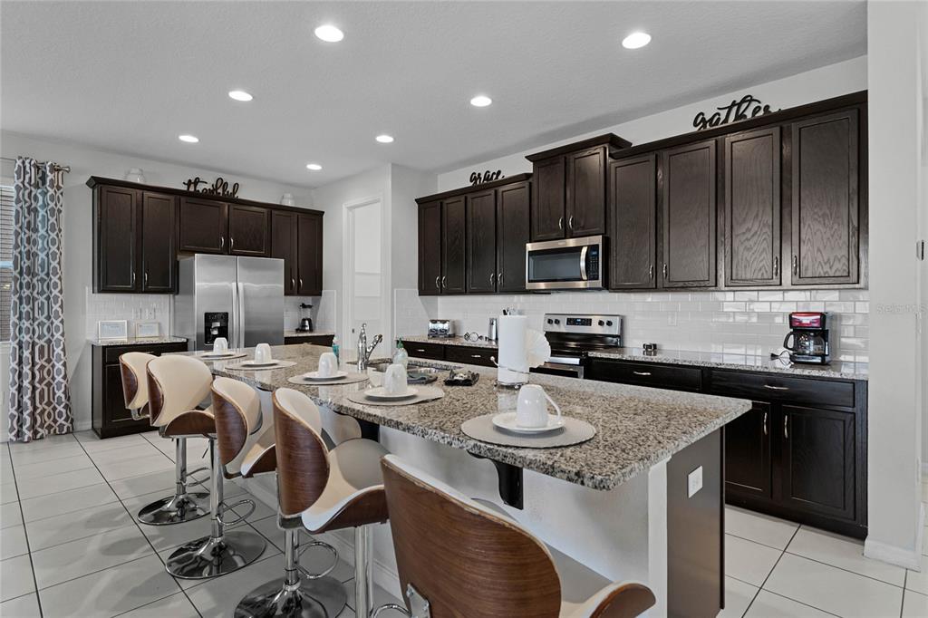 A kitchen features dark wood cabinets, granite countertops, a large island, and stainless steel appliances — 1754 CARIBBEAN VIEW TERRACE, KISSIMMEE, FL