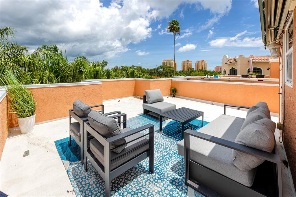 A rooftop terrace features modern patio furniture, a blue patterned rug, and orange stucco walls — 920 NORTH SHORE DRIVE NE, ST PETERSBURG, FL
