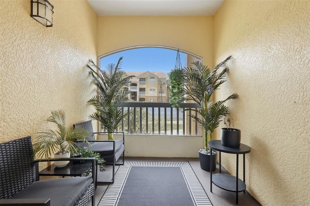 A covered balcony with yellow textured walls, two chairs, potted plants, and a metal railing — 10764 70TH AVENUE UNIT 6104, SEMINOLE, FL
