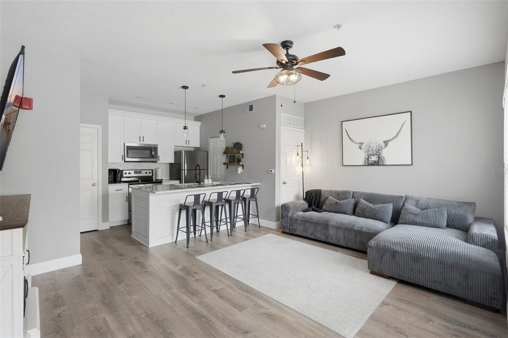 An open-concept living room and kitchen featuring gray flooring, white cabinetry, and a sectional sofa — 10764 70TH AVENUE UNIT 6104, SEMINOLE, FL