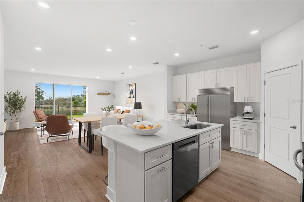 A bright, open-concept kitchen and dining area features white cabinetry, stainless appliances, and wood flooring — 1125 ORANGE TRAILSIDE WAY, OCOEE, FL