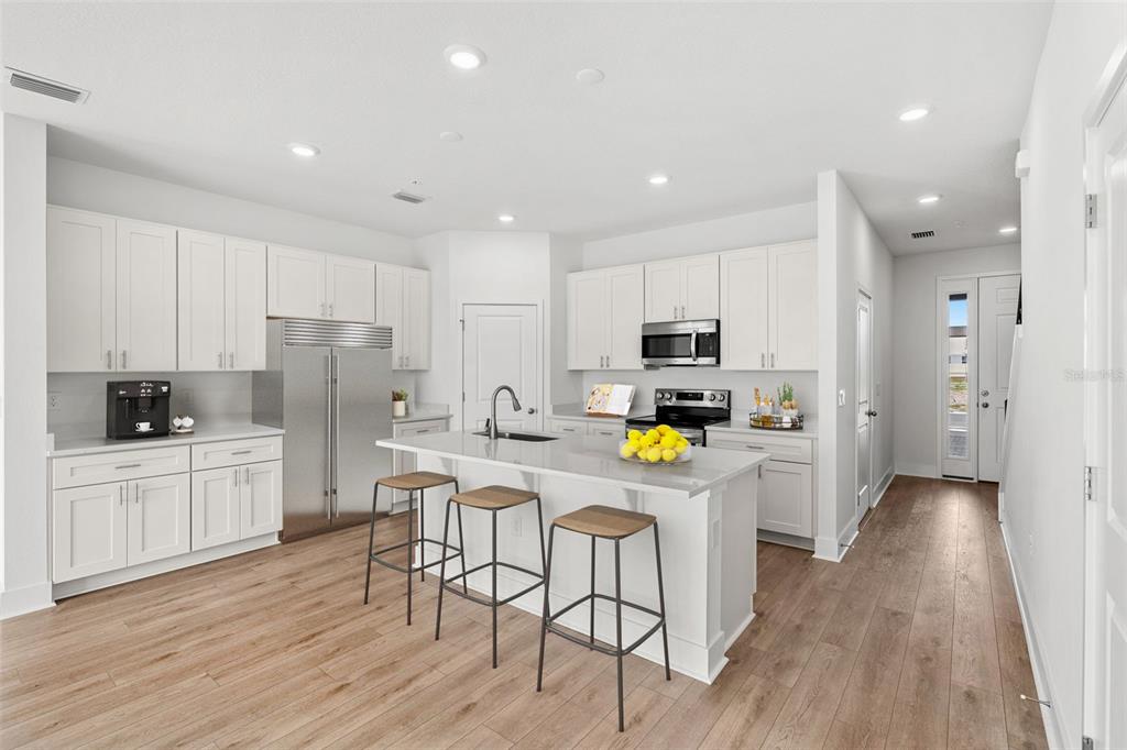 A modern kitchen features white cabinetry, stainless steel appliances, a quartz island, and wood flooring — 1125 ORANGE TRAILSIDE WAY, OCOEE, FL
