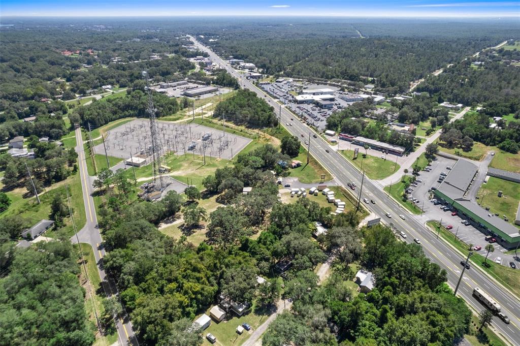 An aerial view shows a power substation, a multi-lane highway, and surrounding wooded commercial properties — 3865-3899 E GULF TO LAKE HIGHWAY, INVERNESS, FL