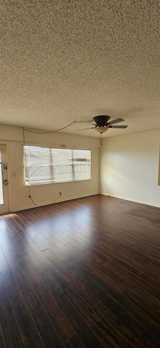 An empty living room features dark wood-look flooring, a popcorn ceiling, and a ceiling fan — 198 E Preston Way # 198, Boca Raton FL 33434, BOCA RATON, FL