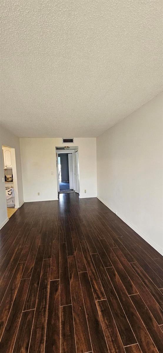 A living room with dark wood-look flooring and a textured ceiling leads to a hallway — 198 E Preston Way # 198, Boca Raton FL 33434, BOCA RATON, FL