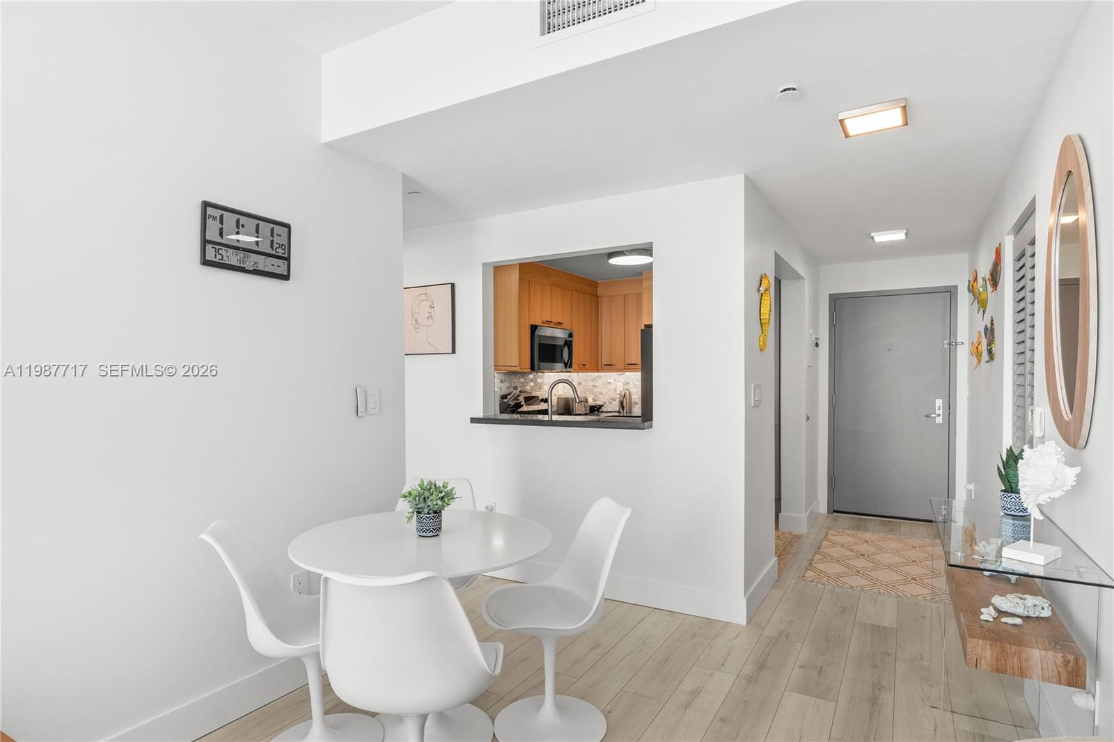 A dining area with a round white table and chairs sits adjacent to a kitchen pass-through — 225 Collins Ave # 5J, Miami Beach FL 33139, MIAMI BEACH, FL