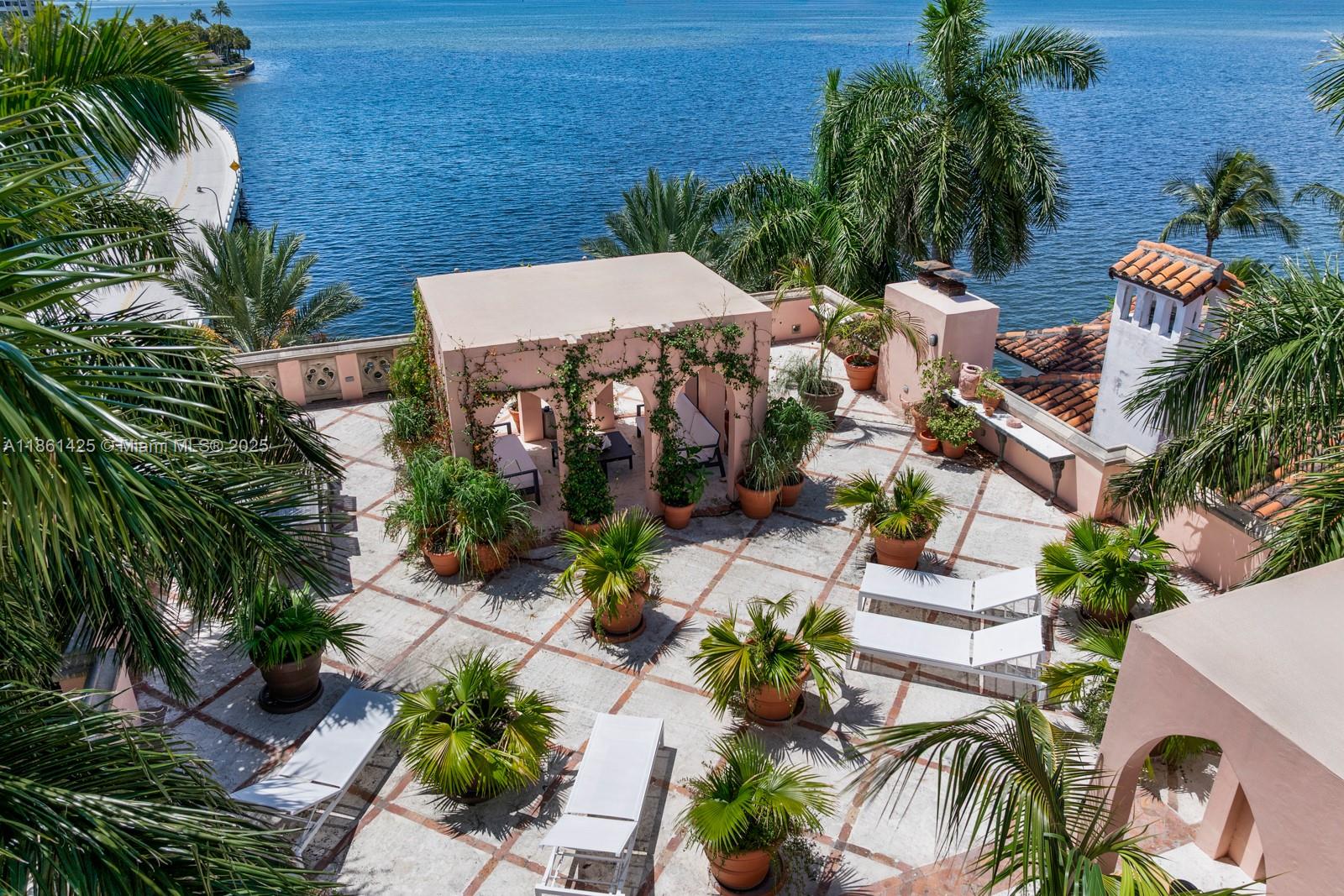 An elevated view of a paved rooftop terrace featuring potted palms, lounge chairs, and a pergola — 1840 S Bayshore Ln, Miami FL 33133, MIAMI, FL