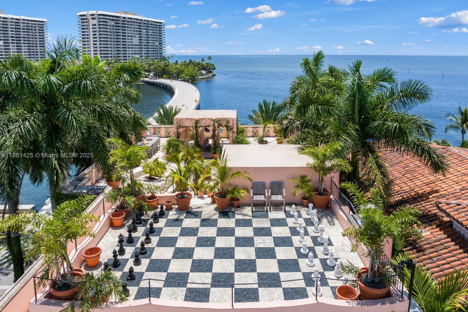 An outdoor rooftop terrace features a large chessboard, potted palm trees, and ocean views — 1840 S Bayshore Ln, Miami FL 33133, MIAMI, FL