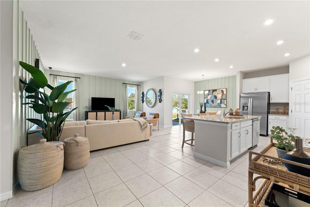 An open-concept living room and kitchen featuring light tile floors and sage green accent walls — 3833 SENNA WAY, TAVARES, FL