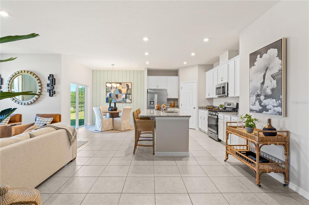 An open-concept kitchen and dining area features white cabinets, a granite island, and tile flooring — 3833 SENNA WAY, TAVARES, FL