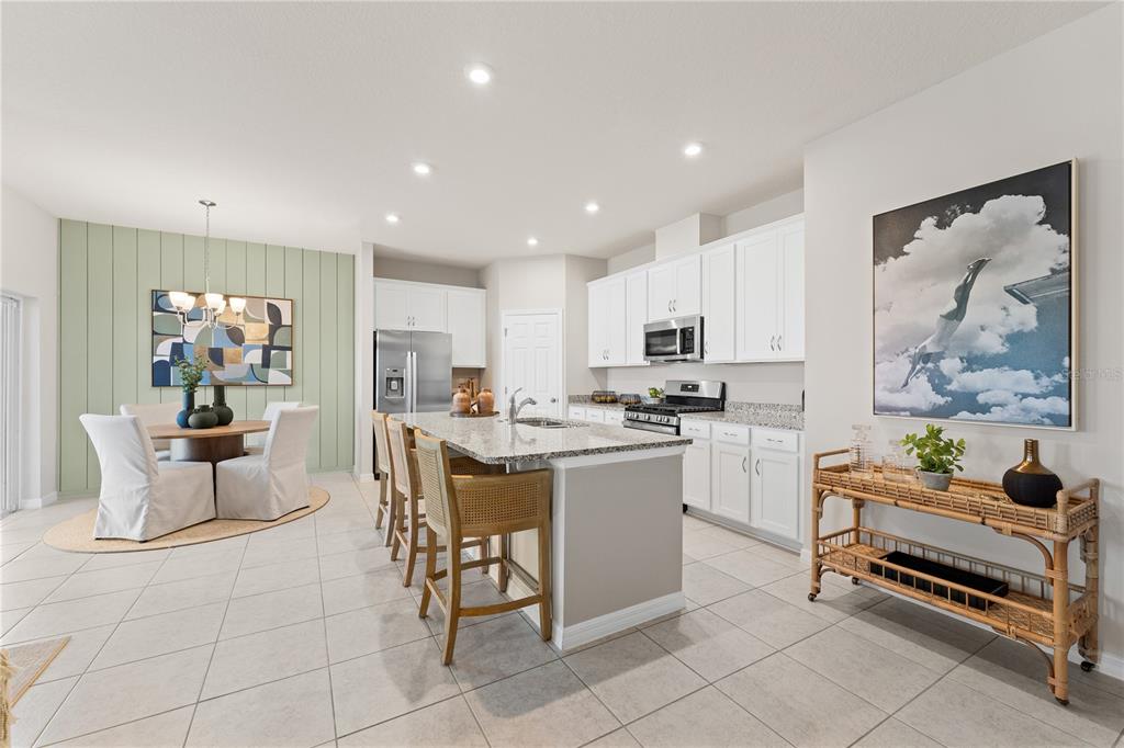 A kitchen with white cabinets, granite countertops, an island, and an adjacent dining area — 3833 SENNA WAY, TAVARES, FL
