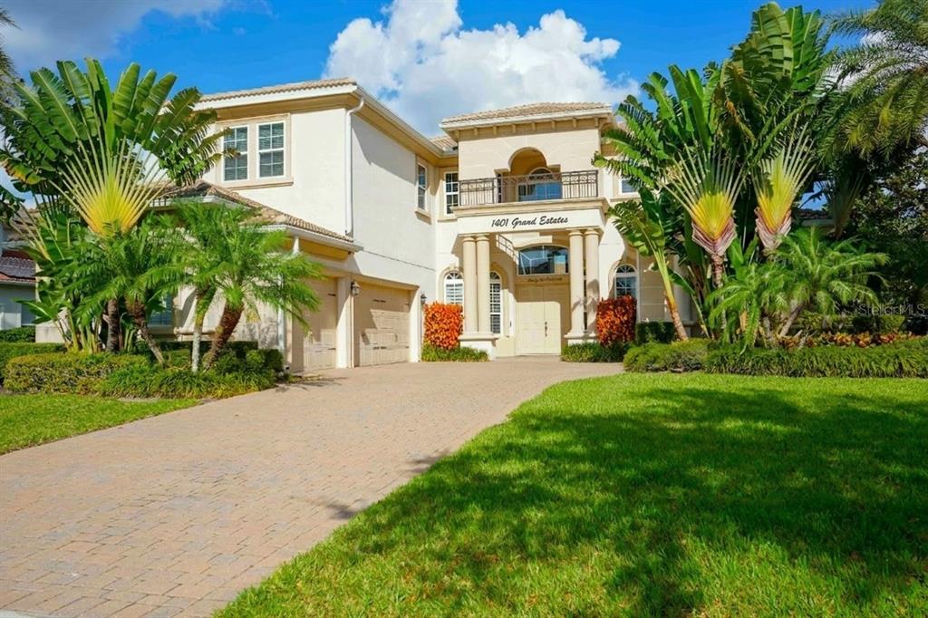 A two-story beige stucco house with a paved driveway and large tropical plants — 6219 TIROCO WAY, WINDERMERE, FL