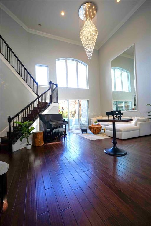 A spacious living room features dark hardwood floors, a grand staircase, and a crystal chandelier — 6219 TIROCO WAY, WINDERMERE, FL