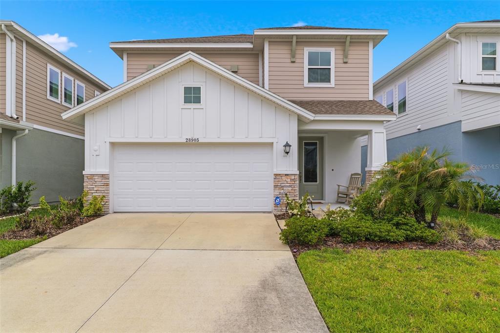 A two-story suburban house with a white garage, stone accents, and a concrete driveway — 28905 ORANGE BERRY DRIVE, WESLEY CHAPEL, FL
