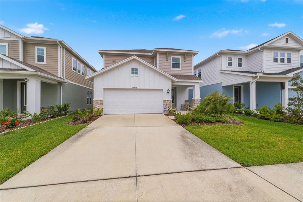 A two-story suburban house with a white garage, tan siding, and a concrete driveway — 28905 ORANGE BERRY DRIVE, WESLEY CHAPEL, FL