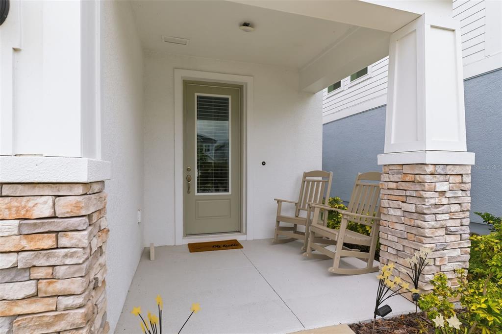 A covered front porch features two rocking chairs, a light green door, and stone pillars — 28905 ORANGE BERRY DRIVE, WESLEY CHAPEL, FL