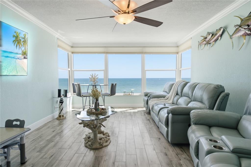 A living room with light blue walls, wood-look flooring, and a large window overlooking the ocean — 14800 GULF BOULEVARD UNIT 303, MADEIRA BEACH, FL