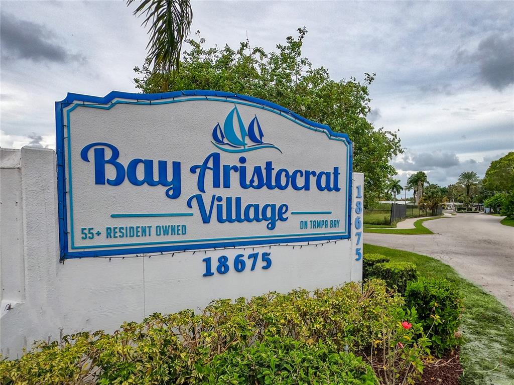 A sign for Bay Aristocrat Village stands in front of a road and green trees — 18675 US HIGHWAY 19 N UNIT 470, CLEARWATER, FL