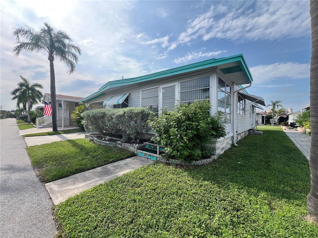 A light-colored mobile home with a screened-in porch and landscaping sits along a paved street — 18675 US HIGHWAY 19 N UNIT 470, CLEARWATER, FL