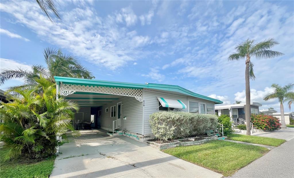 A single-story manufactured home features a teal-trimmed carport, light gray siding, and palm trees — 18675 US HIGHWAY 19 N UNIT 470, CLEARWATER, FL