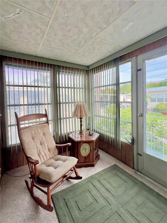 A sunroom features wood-paneled walls, vertical blinds, a rocking chair, and a small wooden table — 18675 US HIGHWAY 19 N UNIT 470, CLEARWATER, FL