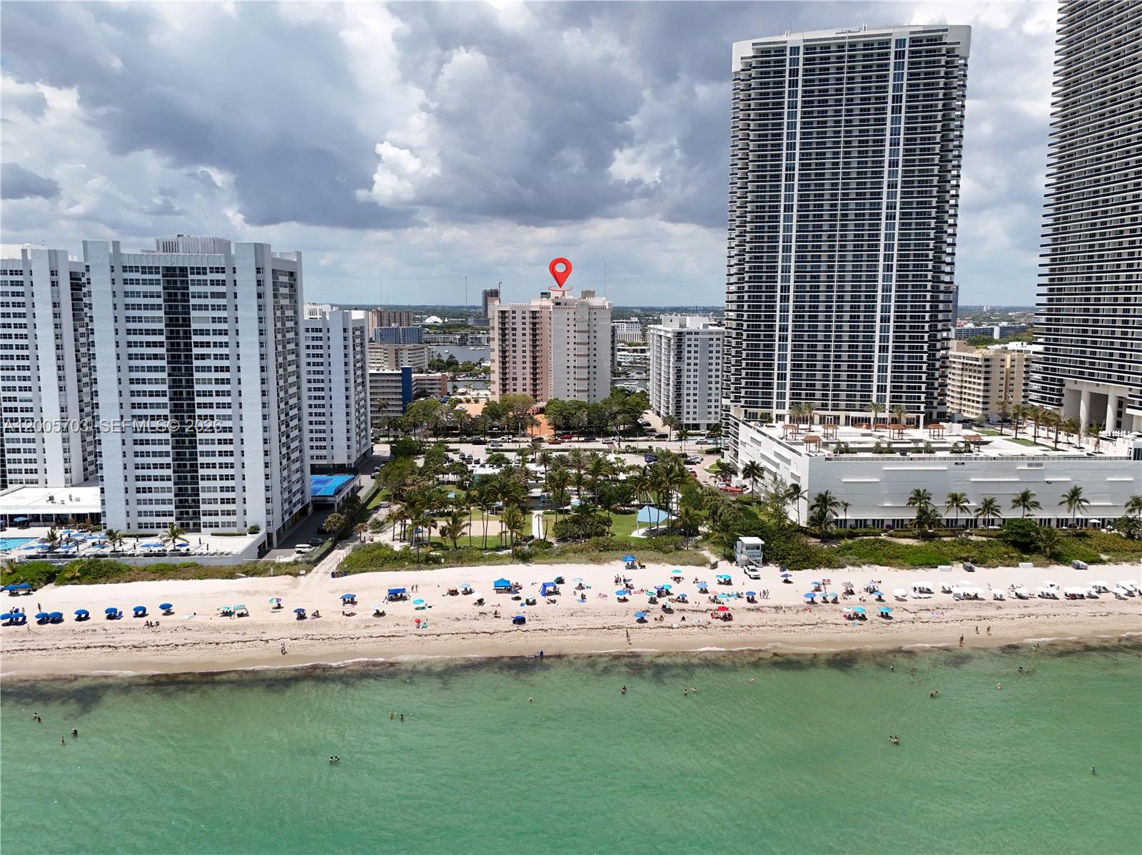 An aerial view shows a sandy beach with people and umbrellas in front of high-rise buildings — 1865 S Ocean Dr # 15B, Hallandale Beach FL 33009, HALLANDALE BEACH, FL