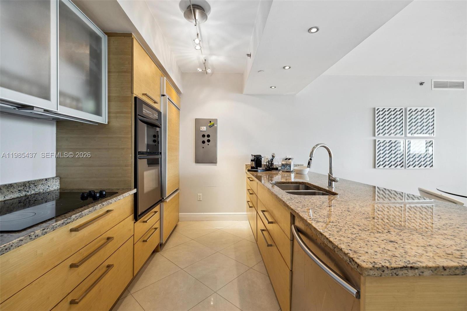 A galley kitchen features light wood cabinets, granite countertops, and stainless steel appliances — 1830 S Ocean Dr # 2703, Hallandale Beach FL 33009, HALLANDALE BEACH, FL