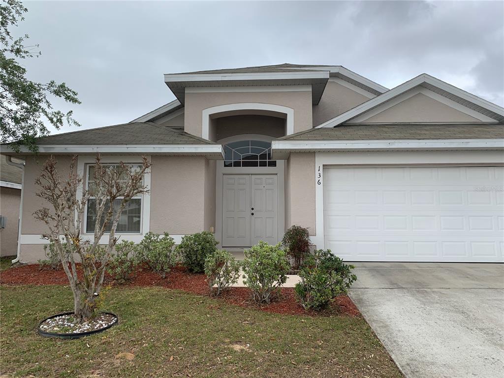 A single-story house with a beige stucco exterior, double front doors, and a two-car garage — 136 GRANTHAM DRIVE, DAVENPORT, FL