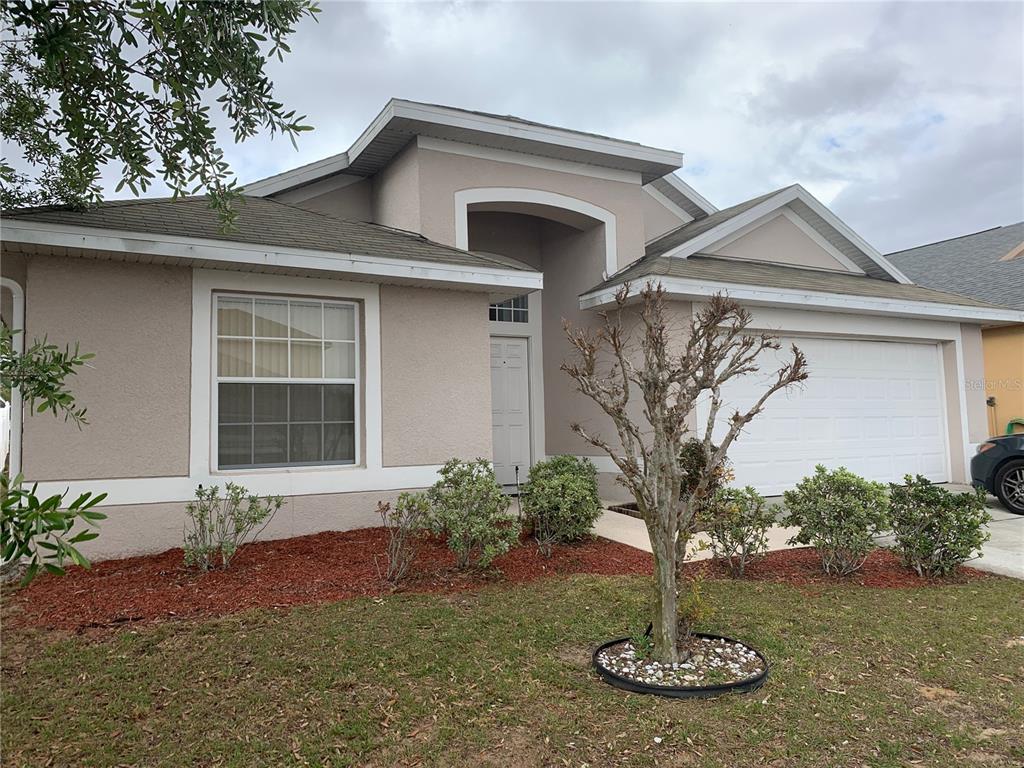A single-story house with a beige stucco exterior, a two-car garage, and a front yard — 136 GRANTHAM DRIVE, DAVENPORT, FL