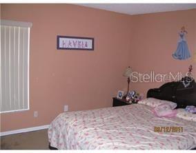 A bedroom features peach walls, a bed with a floral comforter, and vertical window blinds — 136 GRANTHAM DRIVE, DAVENPORT, FL