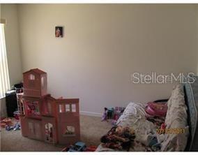 A bedroom features a dollhouse on the carpet and a bed with patterned bedding — 136 GRANTHAM DRIVE, DAVENPORT, FL