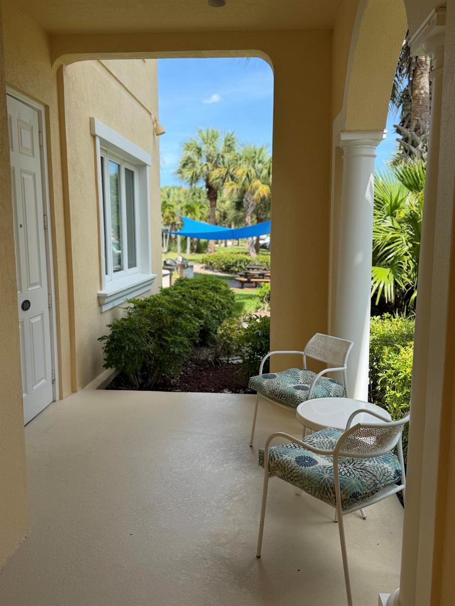 A covered patio features two chairs, a small table, and a view of palm trees — 38 E Harbour Isle Dr Drive E # 106, Fort Pierce FL 34949, FORT PIERCE, FL