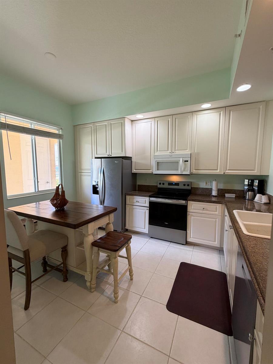 A kitchen features white cabinets, stainless steel appliances, a dark countertop, and a small table — 38 E Harbour Isle Dr Drive E # 106, Fort Pierce FL 34949, FORT PIERCE, FL