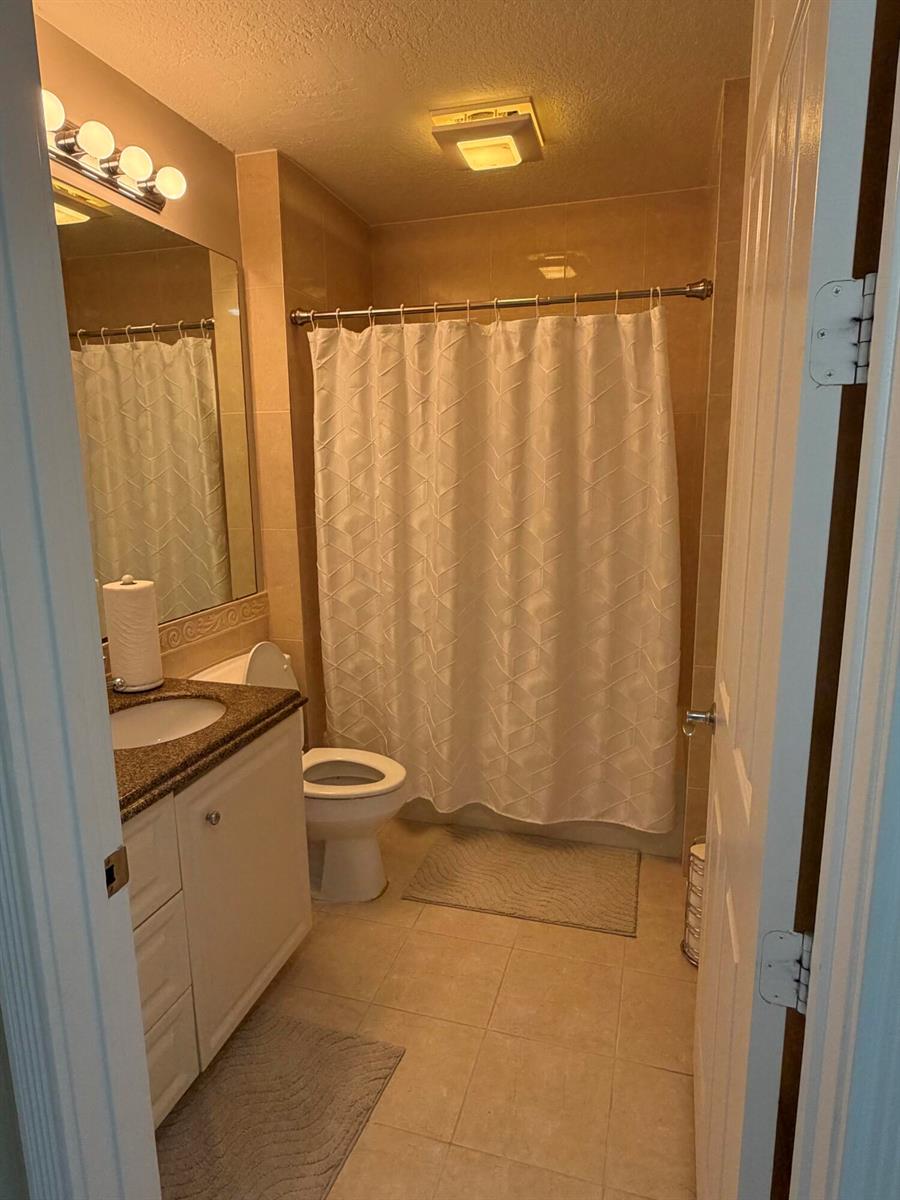 A small bathroom features a white vanity, a toilet, and a shower with a white curtain — 38 E Harbour Isle Dr Drive E # 106, Fort Pierce FL 34949, FORT PIERCE, FL