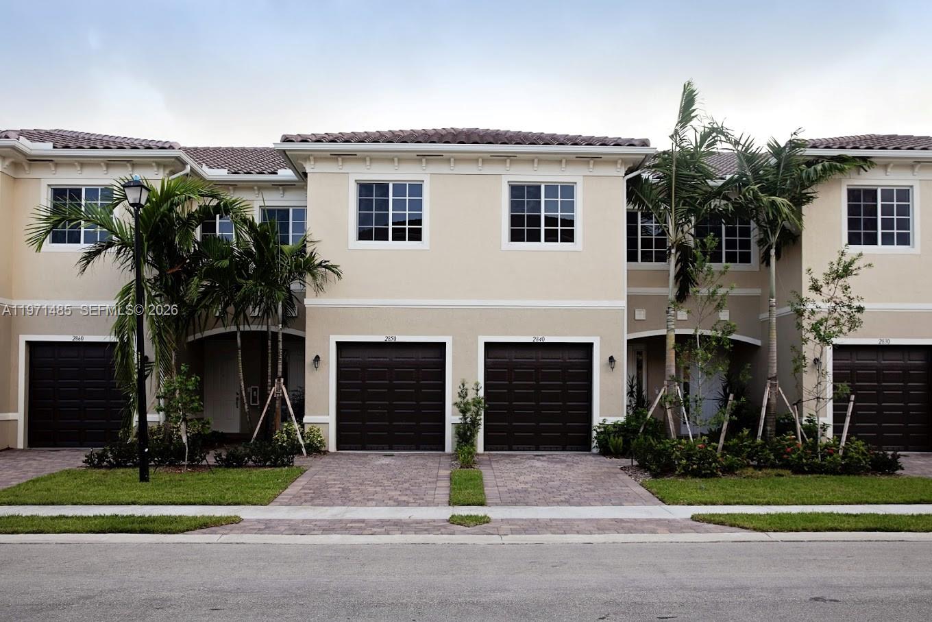 A row of three-story townhouses with beige stucco facades, dark brown garage doors, and palm trees — 2844 SW 81 # 2840, Miramar FL 33025, MIRAMAR, FL