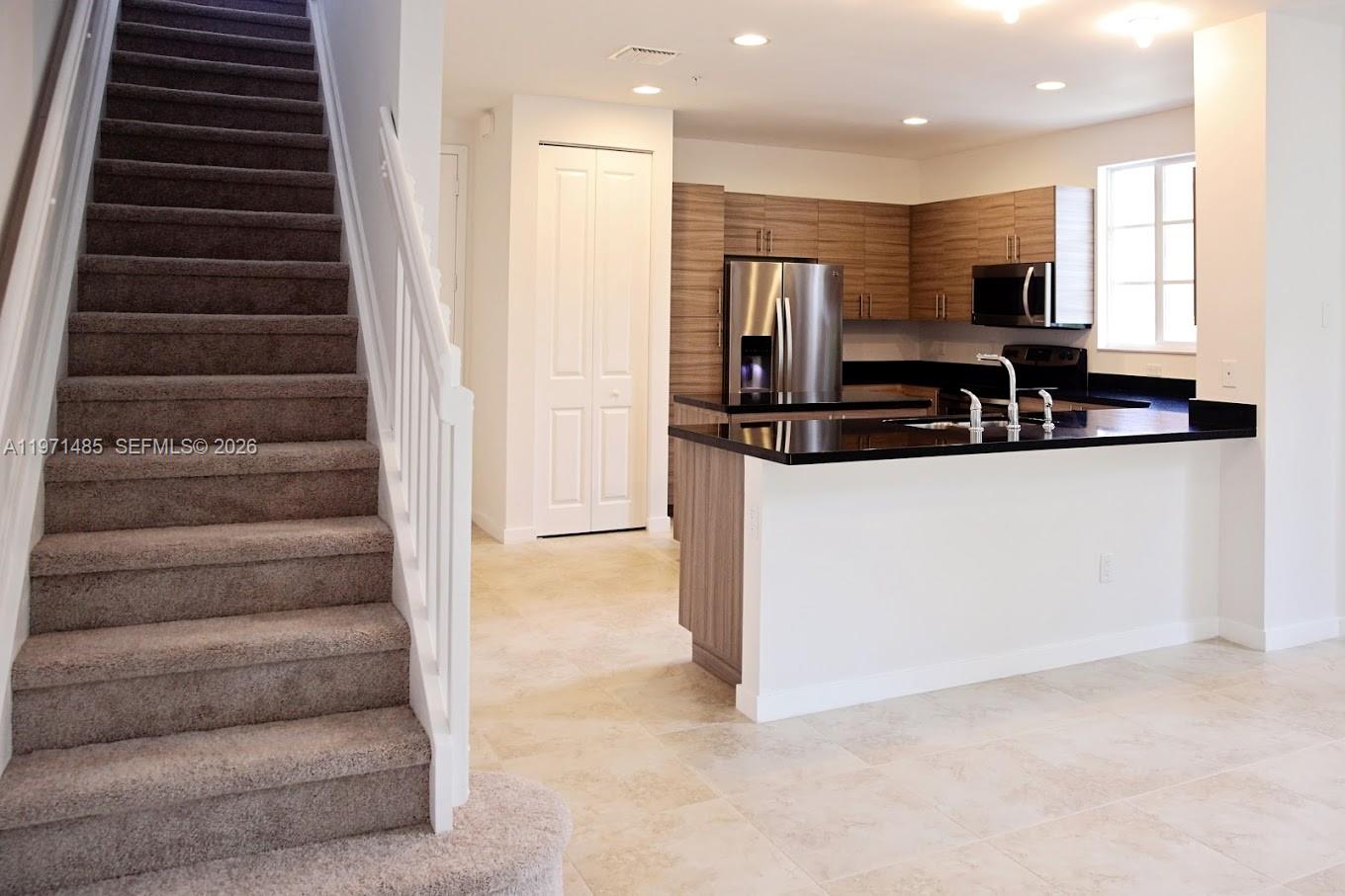 A kitchen with dark countertops and wood-toned cabinets sits beside a carpeted staircase — 2844 SW 81 # 2840, Miramar FL 33025, MIRAMAR, FL
